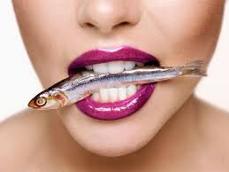 close up of woman's mouth with a sardine in it